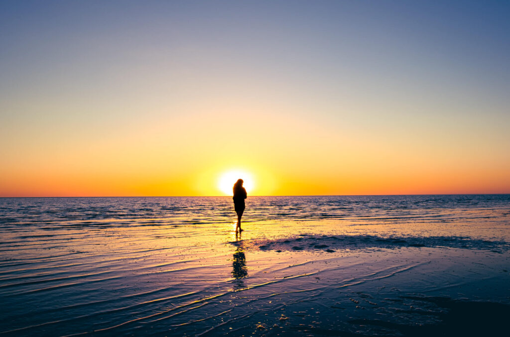 A girl of Icarian tendencies walks out into the ocean and a setting sun